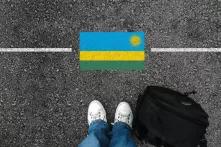 A man with a shoes and backpack is standing on asphalt next to flag of Rwanda and border