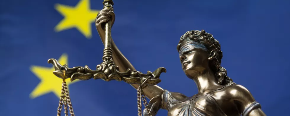 Statue of the blindfolded goddess of justice Themis or Justitia, against an European flag, as a legal concept
