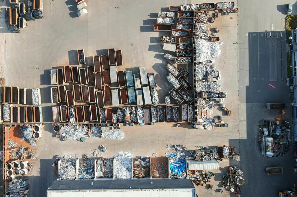 Foto: Luftaufnahme eines Schrottplatzes mit zahlreichen Containern, gefüllt mit Metall- und Aluminiumschrott. Stapel und Haufen von recycelbarem Material.